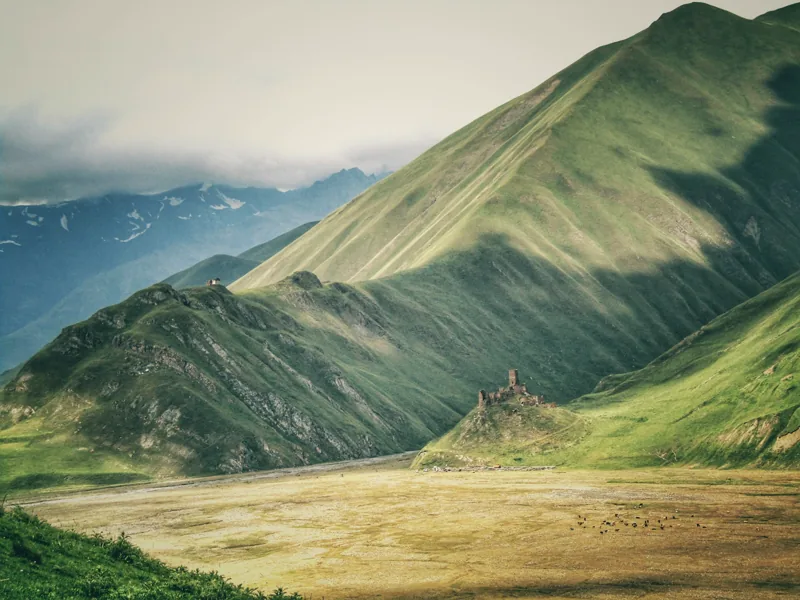 Muted green Caucasus slopes with stone ruins beneath a clouded sky